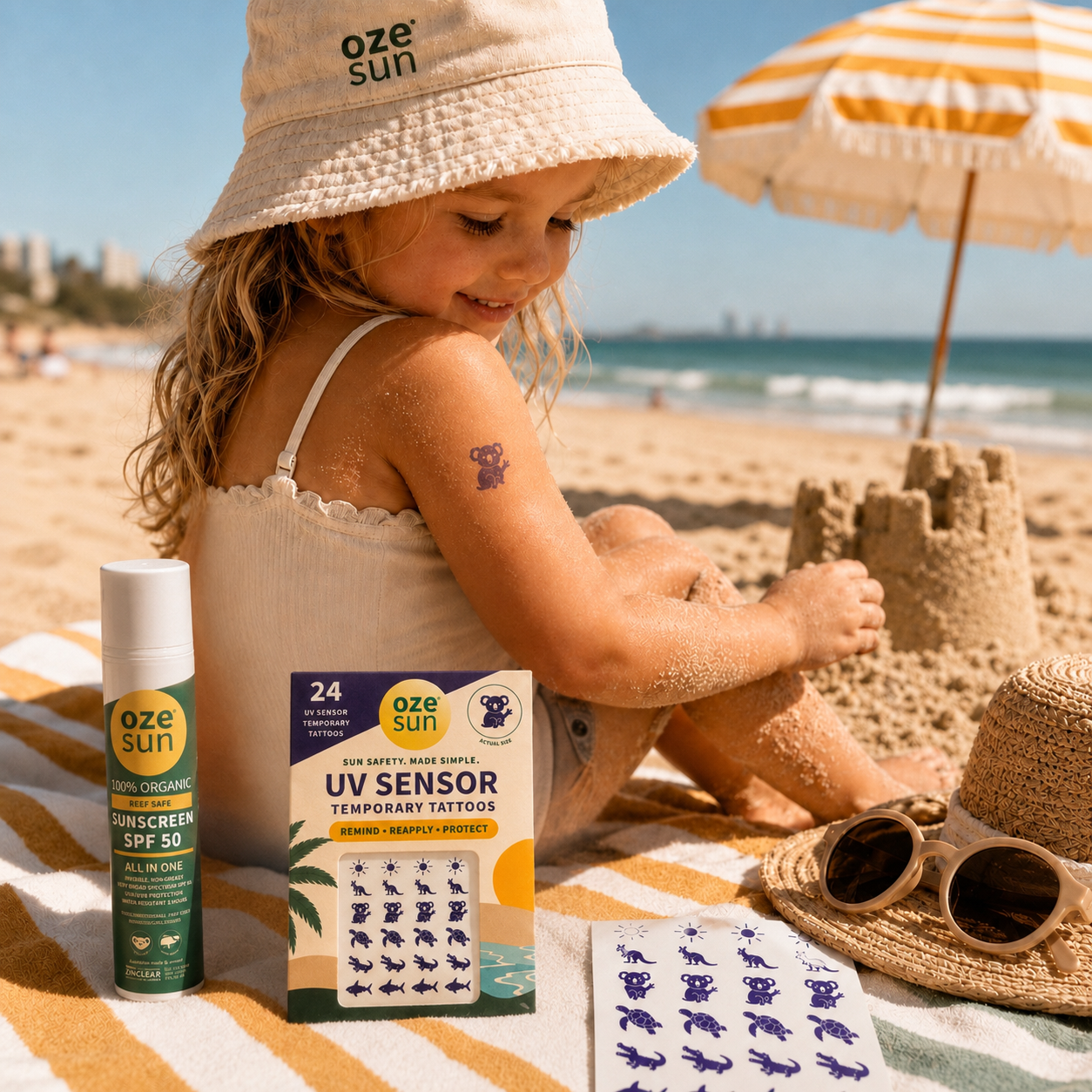 Young girl wearing an Oze Sun bucket hat and purple koala UV sensor temporary tattoo while playing on an Australian beach, beside Oze Sun mineral SPF50 sunscreen and a 24-pack of Australian animal UV sensor temporary tattoos.