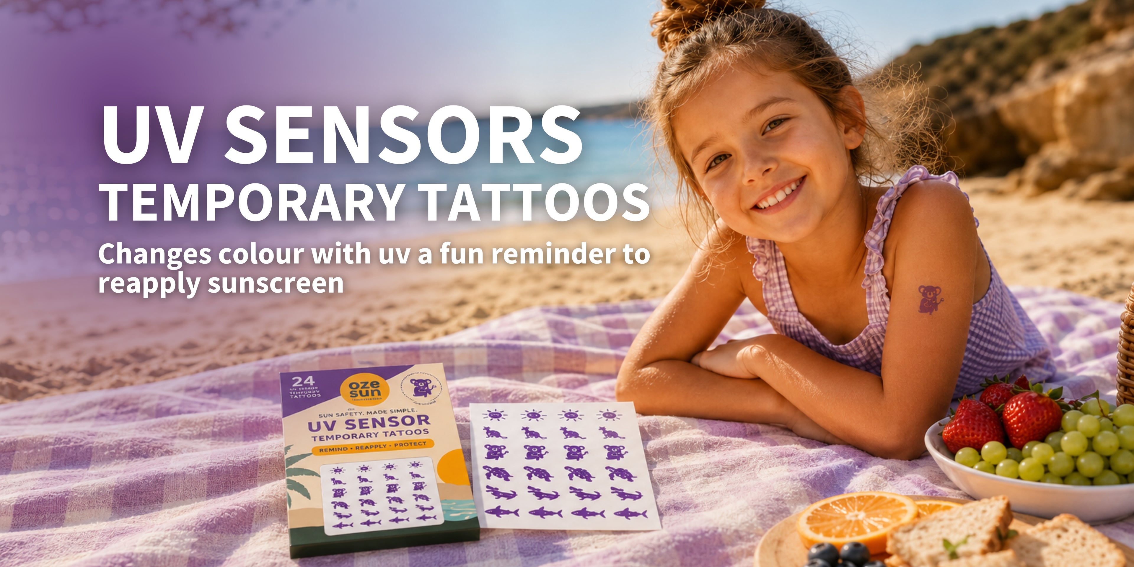 A young girl smiling on a beach picnic blanket with Oze Sun UV sensor temporary tattoos shown in the foreground, alongside a box of UV Sensor Temporary Tattoos and a bowl of fruit.